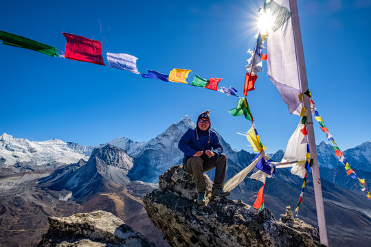 Asian hiker sitting on the cliff in Nangkartsang Peak, Everest Base Camp, with clear blue sky and himalayan mountain range at the background.