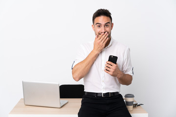 Young business man with a mobile phone in a workplace with surprise facial expression