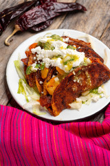 Mexican red enchiladas with potato and pork chorizo also called Potosinas on wooden background