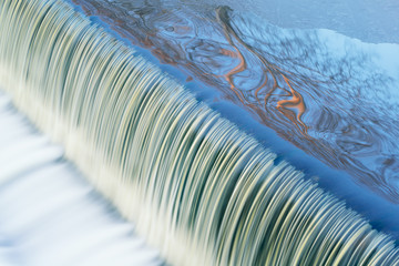 Winter landscape of the Battle Creek River cascade captured with motion blur and with reflections of trees in calm water, Michigan, USA