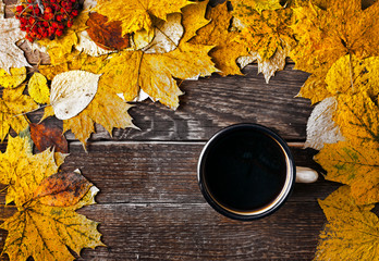 Hot coffee in an enamel mug with autumn maple leaves on wooden background. Autumn cozy background....