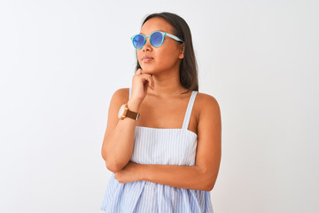 Young chinese woman wearing striped dress and sunglasses over isolated white background with hand on chin thinking about question, pensive expression. Smiling with thoughtful face. Doubt concept.