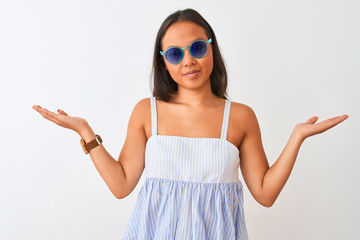 Young chinese woman wearing striped dress and sunglasses over isolated white background clueless...