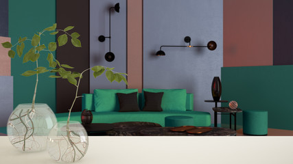 White table top or shelf with glass vase with hydroponic plant, ornament, root of plant in water, branch in vase, house plant, colored lounge with sofa background, interior design