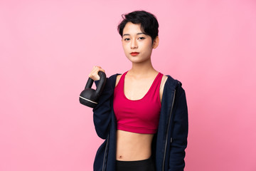 Young sport Asian woman over isolated pink background making weightlifting with kettlebell and looking to the front