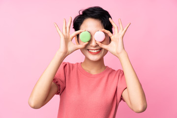 Young Asian girl over isolated pink background wearing colorful French macarons as glasses