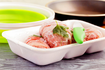 Frozen meat in hoarfrost in a white plastic tray with greens.