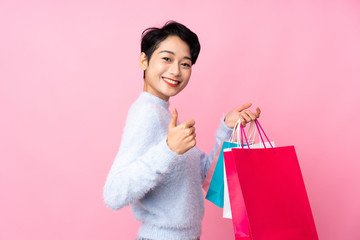 Young Asian girl over isolated pink background holding shopping bags and with thumb up