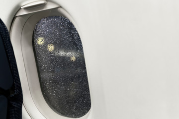 Fototapeta premium Night view from plane illuminator on the airport lights. Scatter of rain are on the porthole glass due to bad rainy weather. Airplane bringing you to tropical countries. Travel concept, copy space.