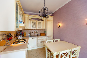 Small cozy kitchen in the style of Provence. Beige furniture, table with chairs, pink walls
