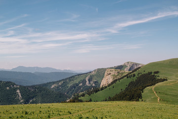 Fototapeta premium View of the mountain meadow and mountain. Beautiful clouds and mountain in a blue haze.
