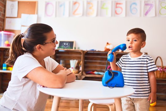 Beautiful teacher and toddler boy playing with vintage blue phone at kindergarten