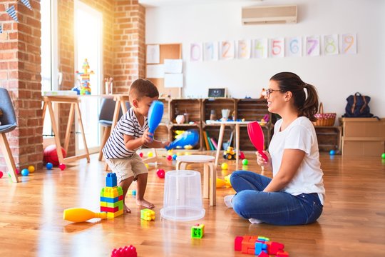 Beautiful teacher and toddler boy playing drum using skitlle and plastic basket at kindergarten