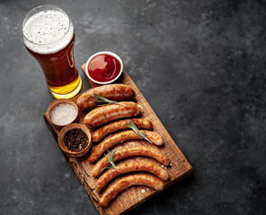 Different grilled sausages with beer with spices on a stone table with copy space for your text
