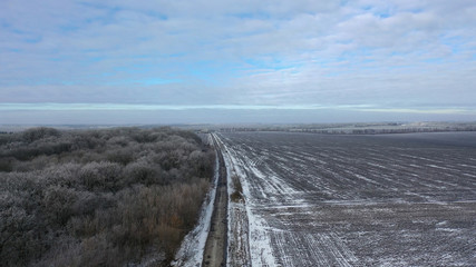 Road, forest and field, first frosts/ Bad road between forest and field. Tree in the yini. Intify in the trees. Winter, snow on the field. The gloomy cold picture of winter