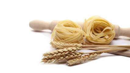 Raw tagliatelle pasta noodles ears wheat and wooden spoon isolated on white background