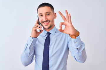 Young handsome business man calling using smartphone over isolated background doing ok sign with fingers, excellent symbol
