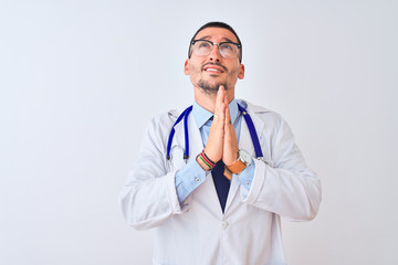 Young doctor man wearing stethoscope over isolated background begging and praying with hands together with hope expression on face very emotional and worried. Asking for forgiveness. Religion concept.