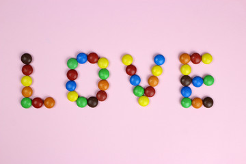 The word love from colored candies on a pink background