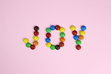 Word joy made of colored candies on a pink background