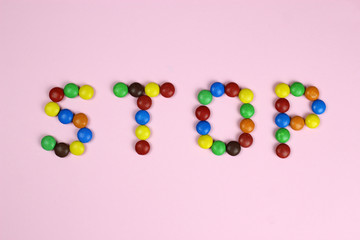 Word stop of multicolored candies on pink background