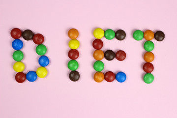 Fototapeta na wymiar Word diet of multicolored candies on pink background