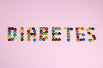 Word diabetes of multicolored candies on pink background
