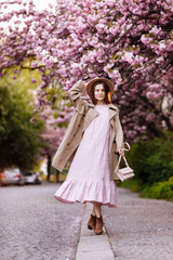 Obraz na płótnie Canvas young beautiful stylish woman in hat and pink dress walking near sakura flowers in the park. Spring concept. Uzhhorod, Ukraine