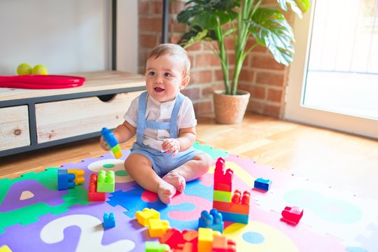 Beautiful toddler sitting on puzzle carpet playing with building blocks at kindergarten