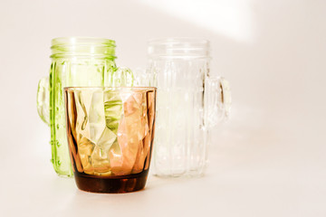 3 glasses - white, brown and green stand on a white background. Sunlight through glass  make a beautiful shade on white background by refraction of light.