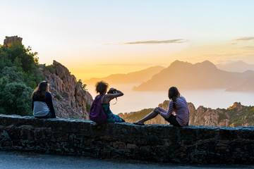 France. Corse. Corsica. Calanques de Piana. Au coucher de soleil, trois touristes admirent le panorama devant elles. : la mer M&eacute;diterran&eacute;e et les rochers. At sunset, three tourists admire the panorama