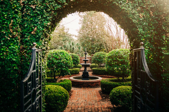 Outdoor Green secret garden with arched entry and gate and a fountain in the middle and red brick and black iron gate