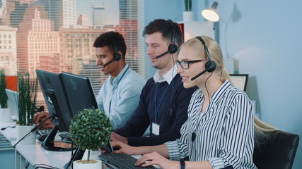 Beautiful female customer service working in busy call center by talking to the international client. Her mixed-race team also taking calls.