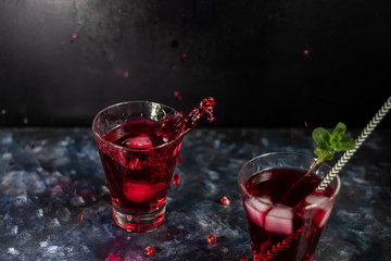 Pomegranate juice in transparent glasses. Spray from a falling piece of ice. On a blue background under a stone. Trend 2020. Grains are scattered nearby.