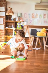 Fototapeta premium Beautiful blonde toddler drawing using digital board around lots of toys at kindergarten
