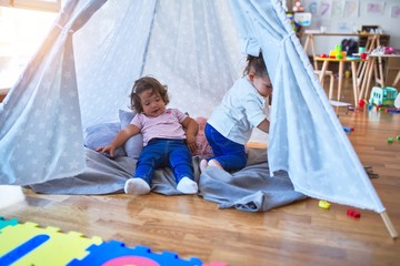 Adorable toddlers lying down over blanket inside tipi smiling at kindergarten