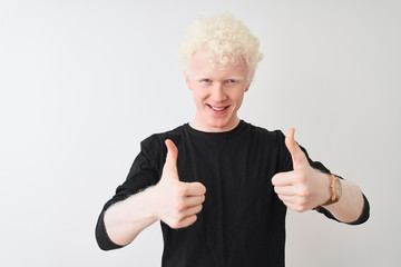 Young albino blond man wearing black t-shirt standing over isolated white background success sign doing positive gesture with hand, thumbs up smiling and happy. Cheerful expression and winner gesture.