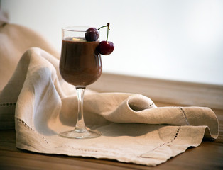 Chocolate mousse, vanilla mousse in a glass with two cherries on the wooden table. Rustic style. Chocolate mousse with whipped cream in a glass on a rustic wooden table. Large glass of latte 