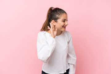 Young brunette girl over isolated pink background listening to something by putting hand on the ear