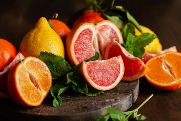Slices of ripe fresh organic citrus fruits: grapefruit, orange, lemon on wooden board. Natural source of vitamins, low calories tasty dessert. Dark background, close up, front view