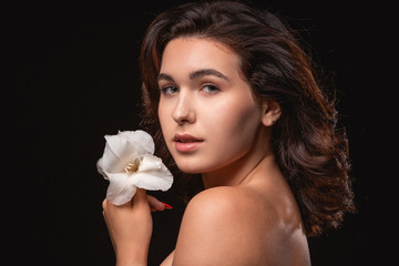 Obraz na płótnie Canvas Beautiful woman with bright makeup posing isolated over black background with white flower.