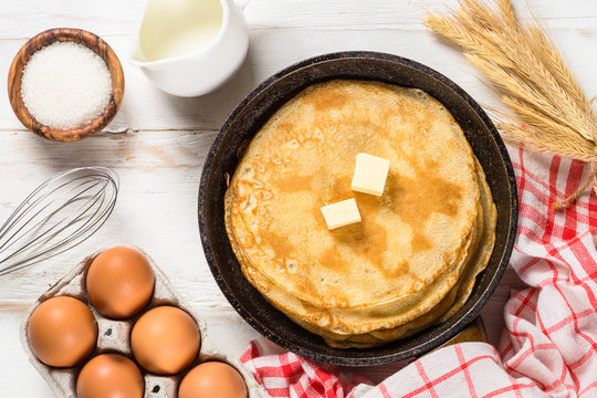 Crepes or thin pancakes in the frying pan with ingredients for cooking.