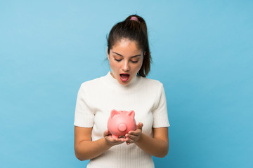 Young brunette girl over isolated blue background holding a big piggybank
