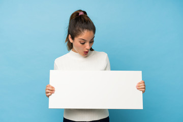 Young brunette girl over isolated blue background holding an empty white placard for insert a concept