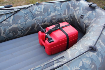 Red plastic fuel tank in bow cockpit of camouflage inflatable motor boat, outdoor water adventure preparation