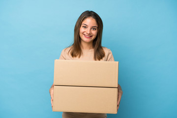 Young brunette girl over isolated blue background holding a box to move it to another site