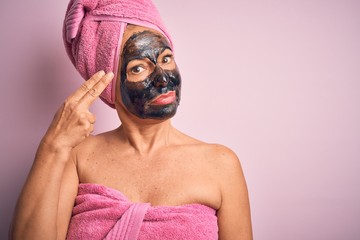 Middle age brunette woman wearing beauty black face mask over isolated pink background Shooting and killing oneself pointing hand and fingers to head like gun, suicide gesture.