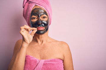 Middle age brunette woman wearing beauty black face mask over isolated pink background mouth and...
