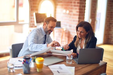 Two middle age business workers smiling happy and confident. Working together with smile on face using laptop at the office