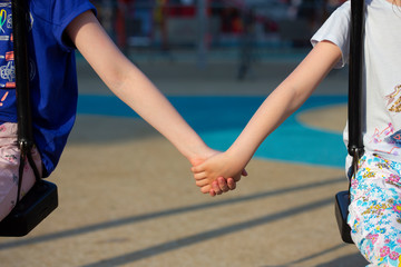 Kids holding hands, sitting on swings on the playground.